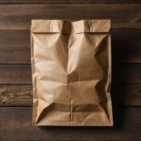 A brown paper bag is sitting on a wooden table. The bag has a few crumpled edges.